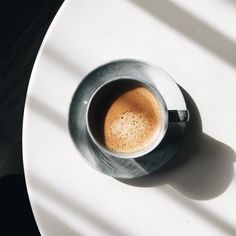 a cup of coffee sitting on top of a white table next to a shadow from the window