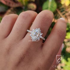 a person's hand with a diamond ring on top of their finger, in front of some leaves