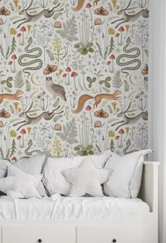 a white bed sitting under a wallpaper covered in animals and plants on top of it