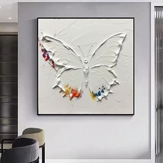 a white butterfly painting hanging on the wall in a living room with chairs and tables