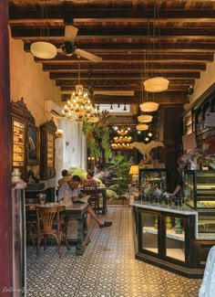 people sitting at tables in a restaurant with chandeliers hanging from the rafters