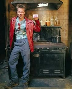 a man standing in front of an old stove holding something up to his right hand