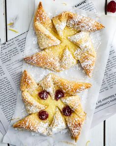 pastries with cherries and powdered sugar sit on top of newspaper paper next to each other