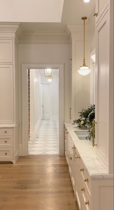 an empty kitchen with white cabinets and wood flooring is seen in this image from the hallway