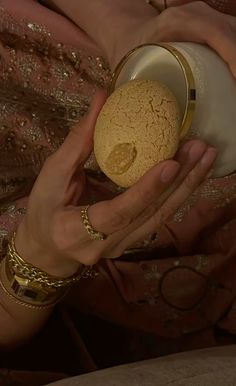 a close up of a person holding an object in their hands and wearing gold bracelets