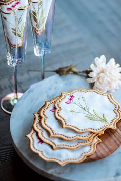 there are four plates with flowers on them and two champagne glasses next to each other