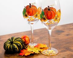 two wine glasses sitting on top of a wooden table next to pumpkins and leaves