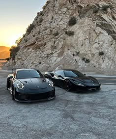 two black sports cars parked next to each other in front of a large rock formation