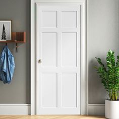 an empty room with a potted plant and coat rack on the wall next to it