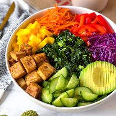 a bowl filled with vegetables and tofu on top of a table next to a fork