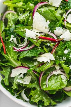 a white bowl filled with green salad and radishes on top of a table