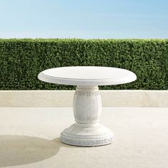 a white table sitting in front of a hedge