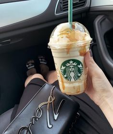 a person holding up a starbucks drink in their hand while sitting in a car with the steering wheel behind them