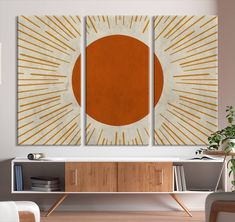 an orange and white painting on a wall in a living room with a wooden sideboard