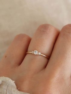 a woman's hand wearing a gold ring with three diamonds on it and the middle finger