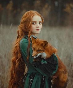 a woman with long red hair holding a fox in her arms and looking at the camera