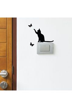 a black cat is sitting on top of a light switch and some butterflies are flying around