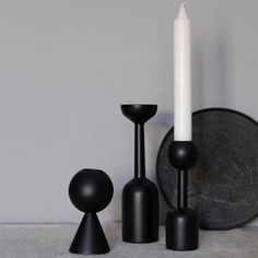 three black candlesticks and one white candle are sitting next to each other on a table