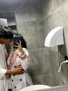 a man and woman standing in front of a bathroom mirror taking a selfie with their cell phone