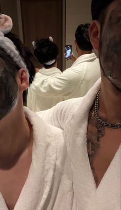 a man in a bathrobe taking a selfie with his cell phone while he is getting ready to shave his hair