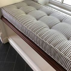 a striped mattress sitting on top of a wooden bench in front of a windowsill