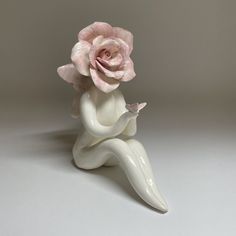 a white vase with a pink flower sitting on it's side and its legs crossed