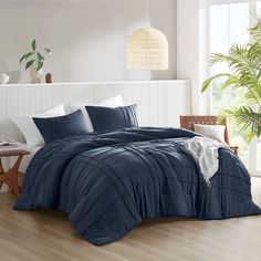 a bed with blue comforters and pillows in a room next to a plant on the floor