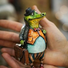 a hand holding a small figurine of a frog wearing an apron and hat