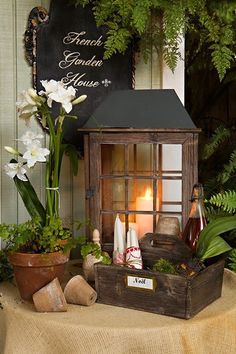 a small wooden lantern sitting on top of a table next to plants and flowers in front of a sign that says grand garden house