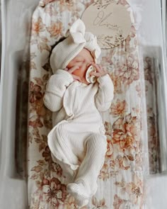 a newborn baby wrapped in a white sweater and bonnet is laying on a floral blanket