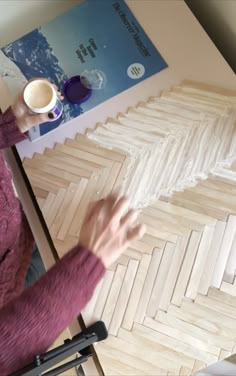 a woman sitting at a table working on some art work with her hands in the air