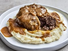 mashed potatoes with gravy and meat on top are served on a white plate