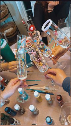 several people are holding up wine glasses with different types of paint and pencils on the table