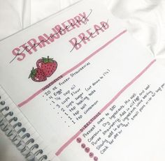 a spiral notebook with strawberry bread written on the side and writing in pink ink next to a white sheet of paper