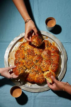 two people grabbing bread from a pan on a table with cups and sauces around them