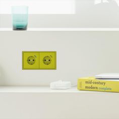 two yellow switches on a white wall next to some books and a vase with flowers in it