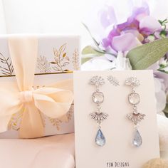 a gift box and two earrings sitting on top of a table next to a card