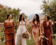 three women in dresses are walking through the grass with flowers on their heads and holding bouquets