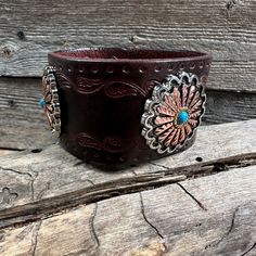 "Brown leather bracelet that has a paisley filigree. It is adorned with antique silver and copper flower pattern with turquoise center western conchos (W220). Measures 7.75\" to 8.25\" with two snaps to create two sizes." Southwestern Style Brown Concho Bracelets, Vintage Concho Leather Bracelet For Festival, Vintage Leather Concho Bracelet For Festival, Brown Bohemian Leather Bracelet With Concho, Western Style Leather Bracelet With Concho, Western Style Leather Bracelet With Concho As Gift, Western Leather Jewelry With Concho, Western Style Leather Concho Bracelet As Gift, Western Style Brown Cuff Bracelet For Festivals