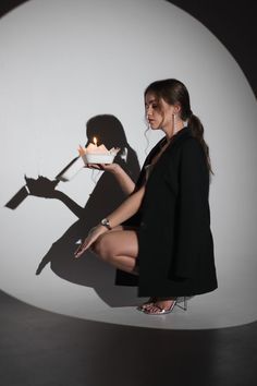 a woman holding a cake with a candle on it in front of a white wall