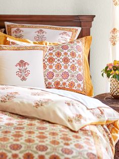 a bed with orange and yellow pillows on it next to a vase filled with flowers