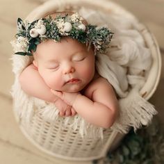 a baby sleeping in a basket wearing a flower crown