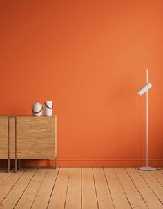 an orange wall with two white lamps and a wooden cabinet in the middle, against a wood floor