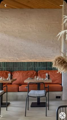 the interior of a restaurant with orange couches and tables in front of a stone wall