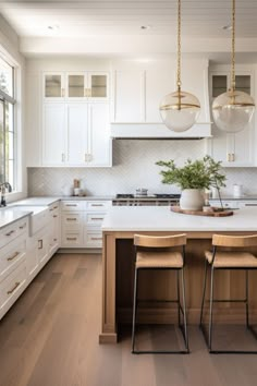 a kitchen with white cabinets and counter tops next to two stools in front of an island