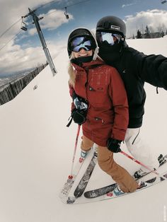 two people standing on skis in the snow with goggles on and one person is holding his arm around the other