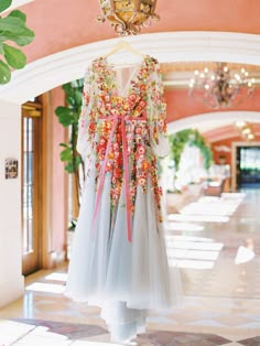 a dress hanging on a rack in a room with chandelier and potted plants