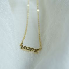 This elegant "hope" necklace is a symbol of positivity and strength. Crafted from high-quality 14k gold plated silver, it features a unique design with a center piece and two loops on either side. The necklace is 16 inches in length with a 1-inch extension, allowing for adjustable wear. Finished with a lobster clasp, this necklace is both stylish and versatile, making it a perfect addition to any outfit. Details: Material: 14k gold plated silver  Necklace length: 16 inches with 1-inch extension Design: "HOPE' is 20mm long 5mm wide and 1mm thick  Closure: Lobster clasp Hypoallergenic: Yes Nickel-free: Yes Handcrafted: Yes Hope Necklace, Extension Designs, Necklace Layering, Gold Necklace Layered, Layering Necklace, Gold Plated Silver, 14kt Gold, Necklace Length, Outfit Details