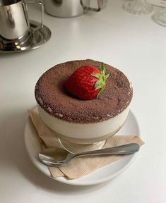 a chocolate cake topped with a strawberry on top of a white plate next to silverware