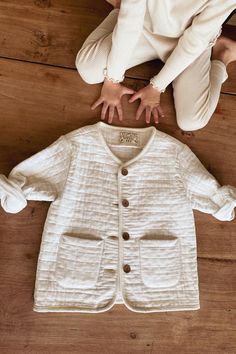 a baby laying on the floor next to a white shirt and jacket with hands in it